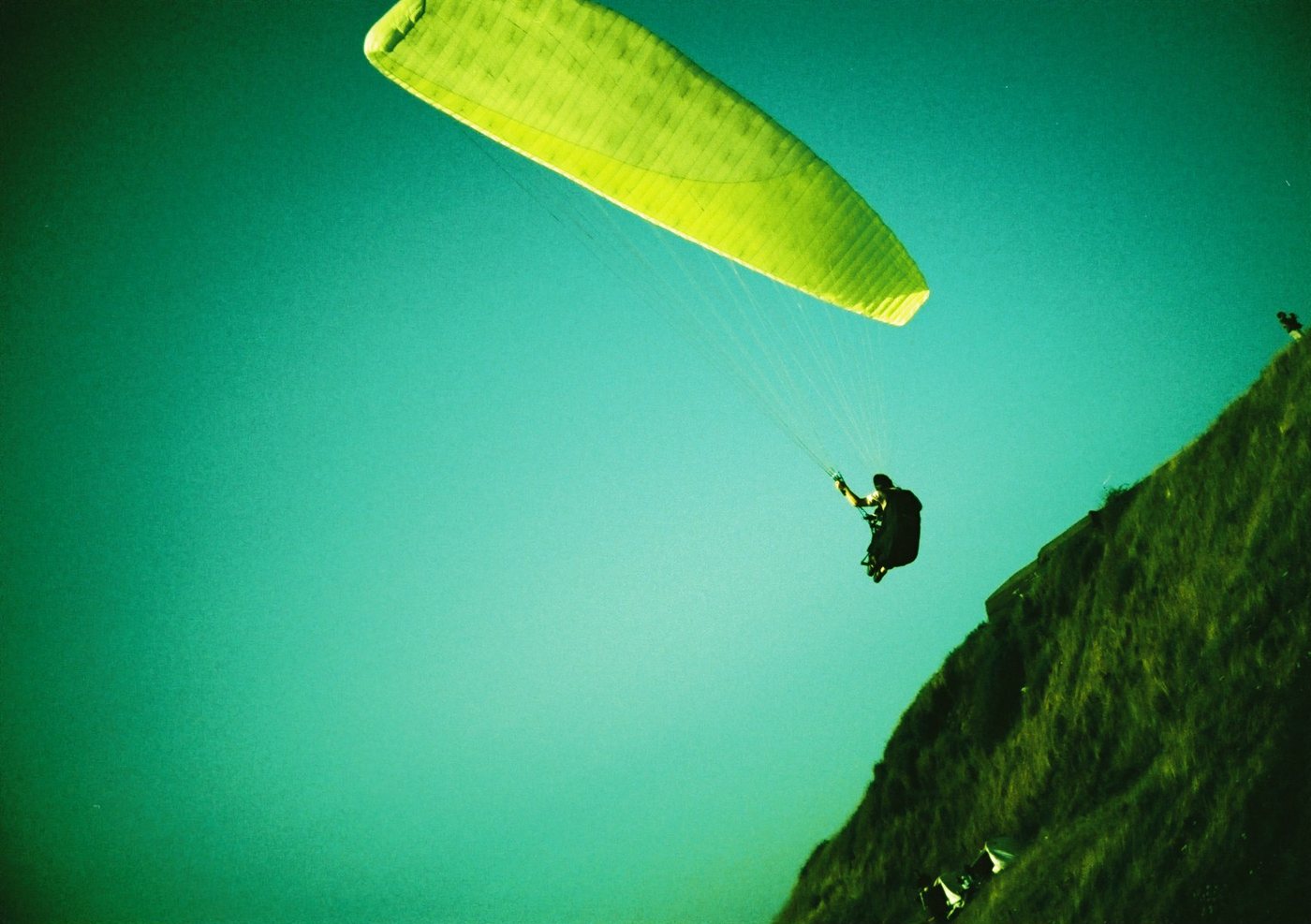 Paraglider mit gr&uuml;n-gelber Kappe vor t&uuml;rkisem Himmel (Lomo, Belgien)