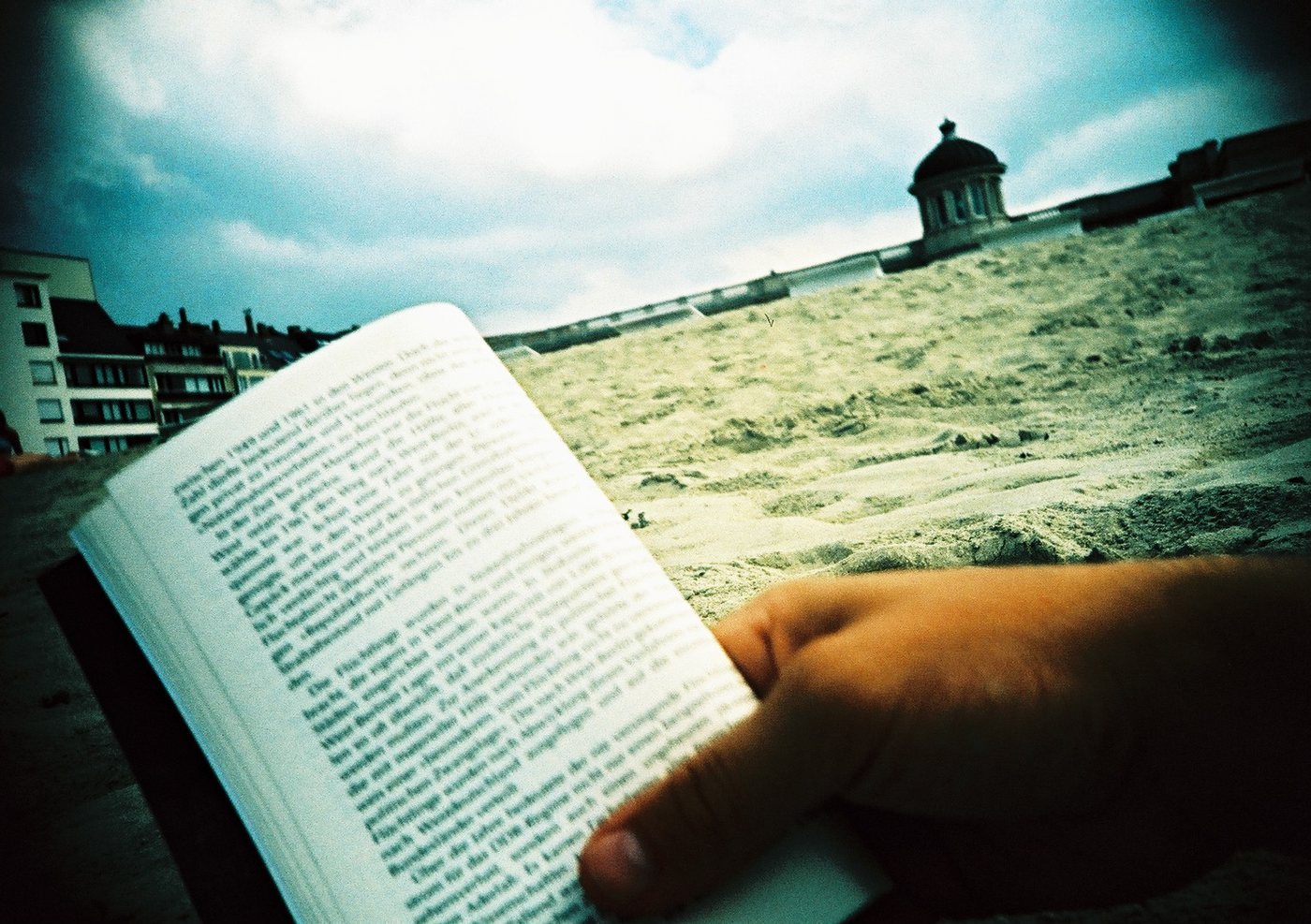 Hand mit aufgeschlagenem Buch am Strand (Lomo, Belgien)