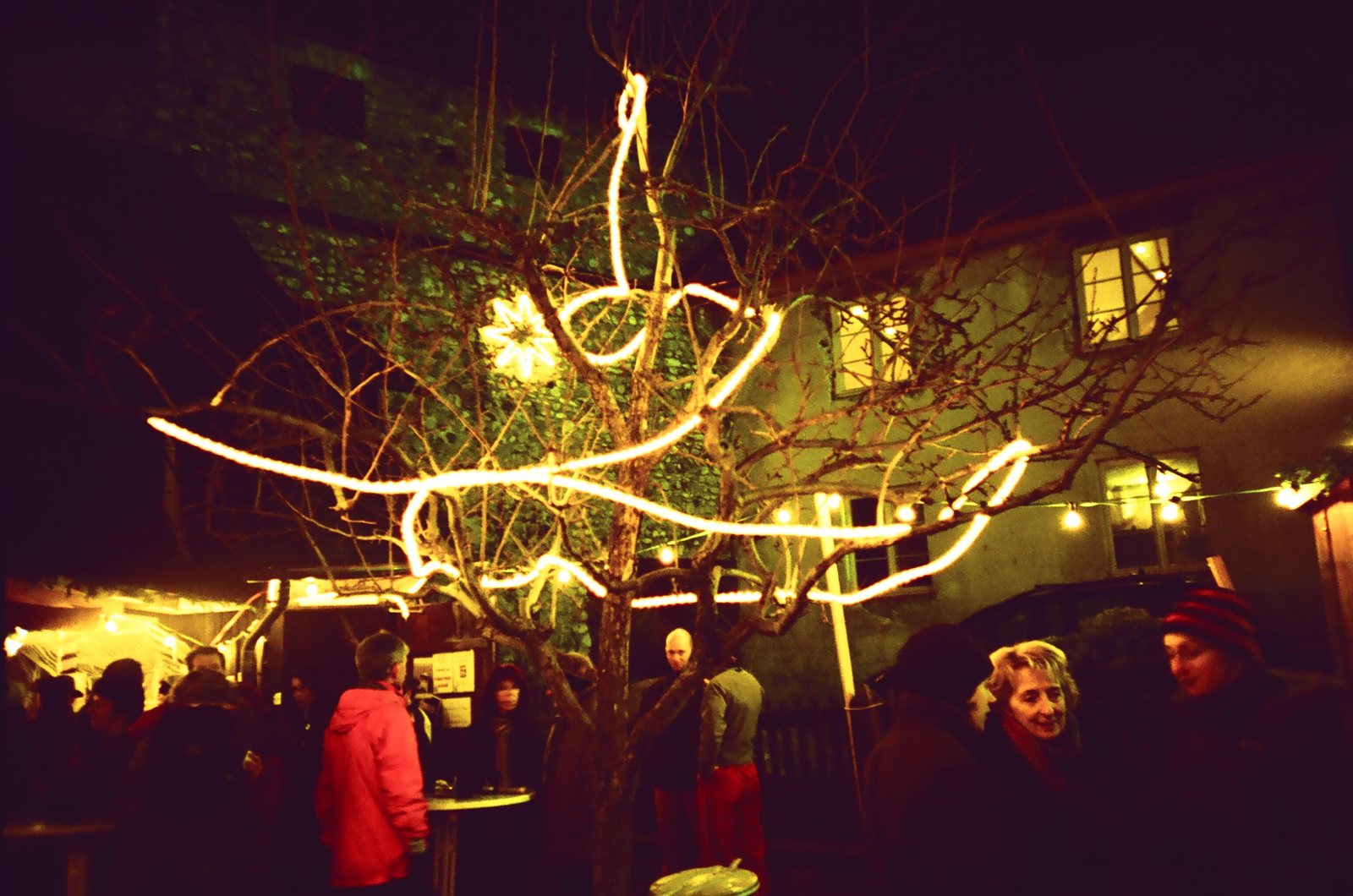Innenhof am Abend mit Lichterketten und Menschen im Gespräch (Lomo)